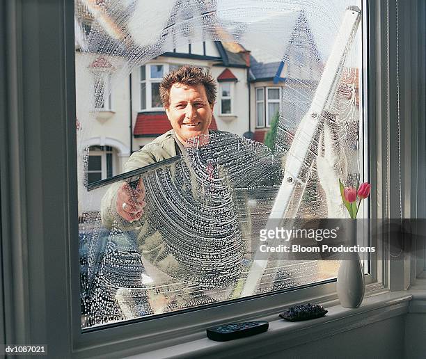 portrait of a window cleaner looking through and cleaning a window - window cleaning stock pictures, royalty-free photos & images