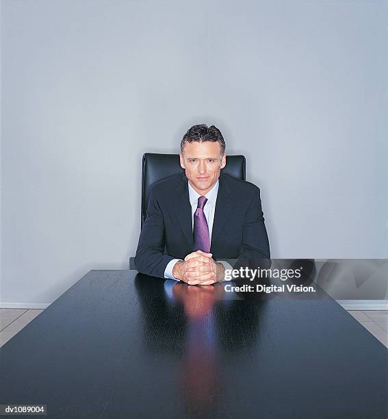 portrait of a mature ceo sitting at the end of a long table with his hands clasped together - ojos grises fotografías e imágenes de stock