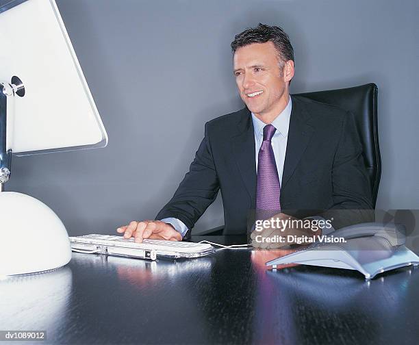 mature ceo sitting at his desk and using his computer - ojos grises fotografías e imágenes de stock