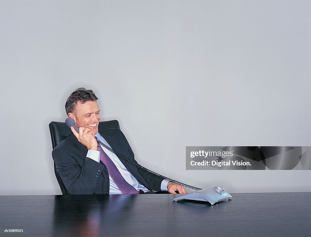 Smiling, Mature CEO Using the Phone Sitting at His Desk