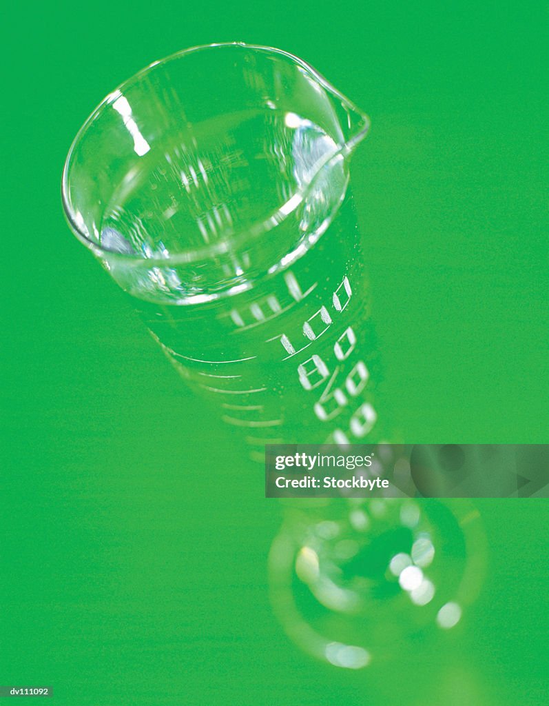 Graduated cylinder filled with clear liquid, against green background
