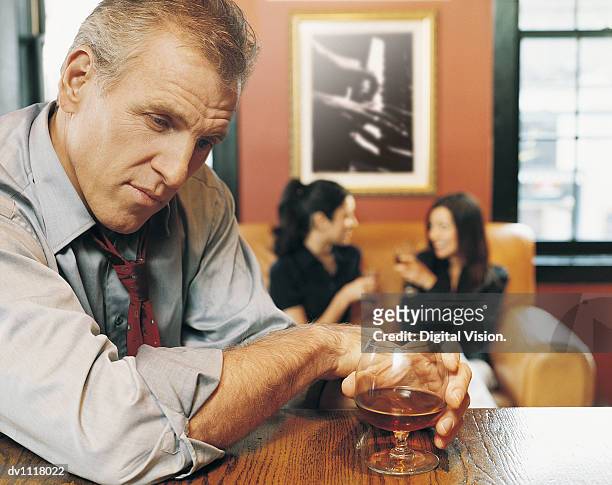 portrait of a drunk businessman leaning on a bar counter with business people in the background - konjaksglas bildbanksfoton och bilder