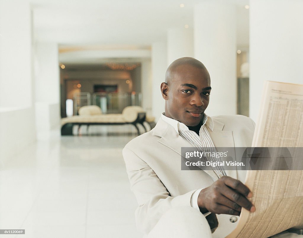 Portrait of a Stylish Businessman Sitting in a Hotel Lobby Holding a Newspaper