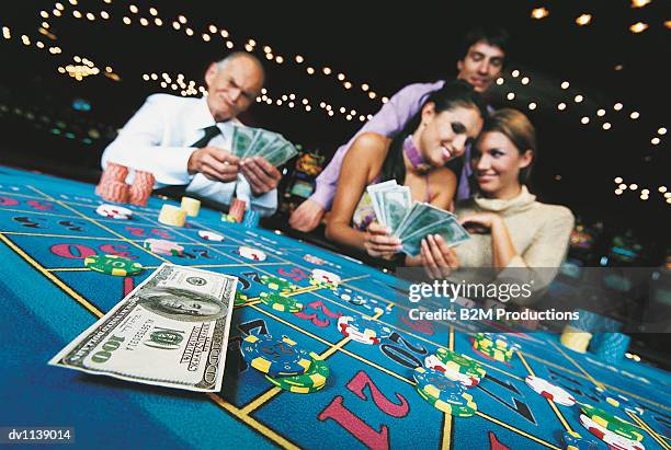 four people gambling with hundred dollar banknotes at a casino table - gambling table stock pictures, royalty-free photos & images