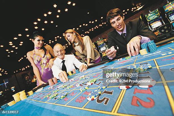 two men arranging their gambling chips on a casino table with two young women watching the senior man - gambling table 個照片及圖片檔