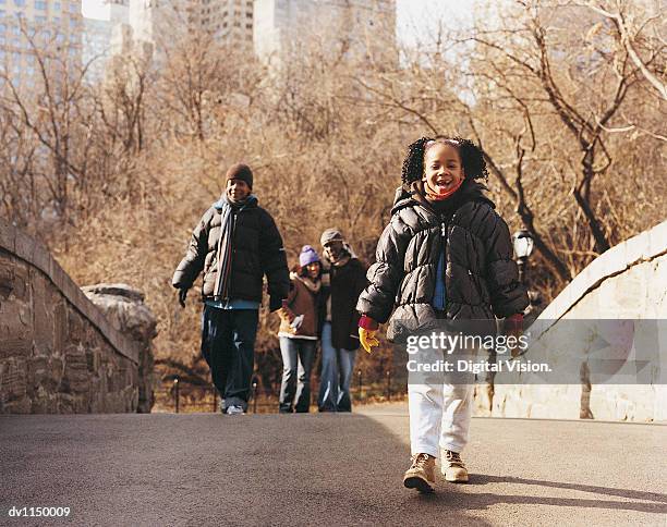 portrait of a young girl walking across a bridge with her family in an urban park in autumn - child winter coat stock pictures, royalty-free photos & images