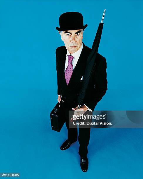 portrait of a grumpy old businessman with a bowler hat, briefcase and umbrella - hat and suit stock pictures, royalty-free photos & images