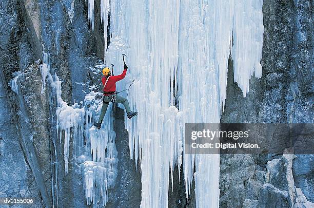 adult using an ice axe and crampons to climb up an icy rock face - ice climbing stockfoto's en -beelden