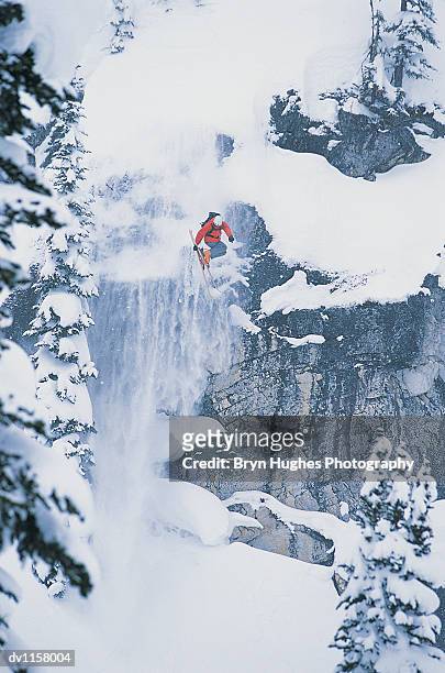 skier jumping mid air off a steep rock face in a forest - face off sports play - fotografias e filmes do acervo