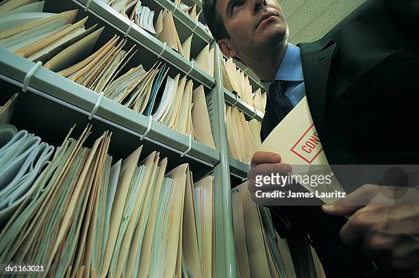 businessman taking a confidential file from a filing cabinet - file cabinet stock-fotos und bilder