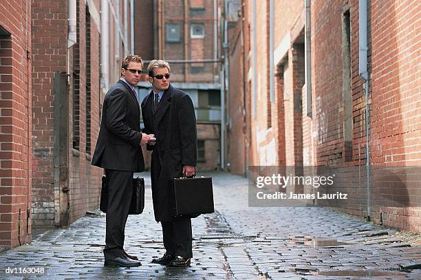 suspicious businessmen standing in a backstreet giving and receiving a bundle of money - list stock-fotos und bilder