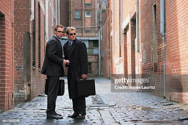 suspicious businessmen standing in a backstreet giving and receiving a bundle of money - contact list stock-fotos und bilder