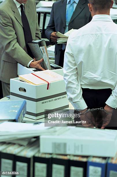 businessman standing in an office wearing handcuffs and businessmen searching through folders and documents - searching for something ストックフォトと画像