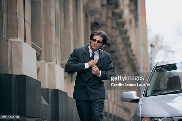 businessman walking in the city hiding a parcel in his suit - suspicious package stock pictures, royalty-free photos & images