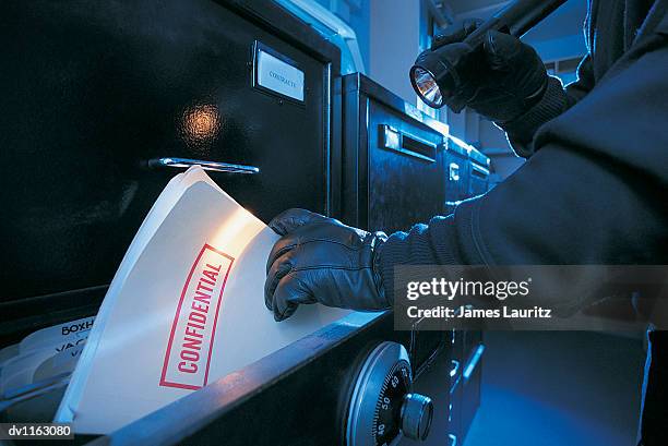 robber stealing a confidential file from an open filing cabinet - file cabinet stock-fotos und bilder