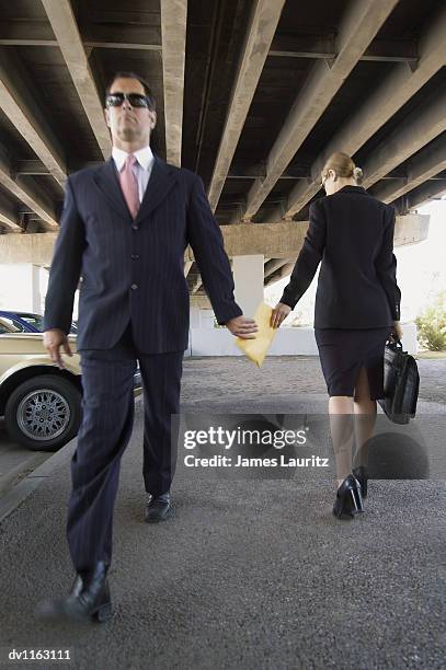 suspicious businessman passing an envelope to a businesswoman in a car park below an underpass - suspicious package stock pictures, royalty-free photos & images