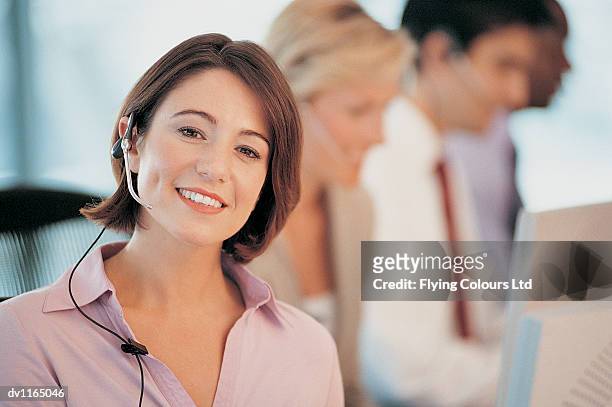 portrait of a young businesswoman wearing a headset sitting in an open plan office - open blouse stock-fotos und bilder