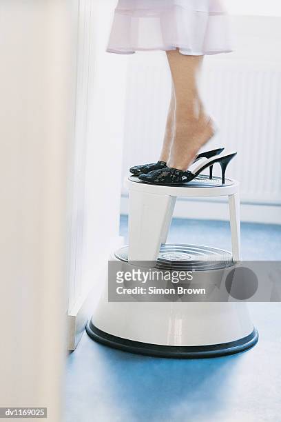 close up of a businesswoman standing on tiptoe on a step stool in an office - step stool imagens e fotografias de stock