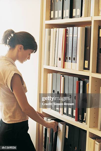 businesswoman searching through ring binders on shelving in an office - searching for something ストックフォトと画像