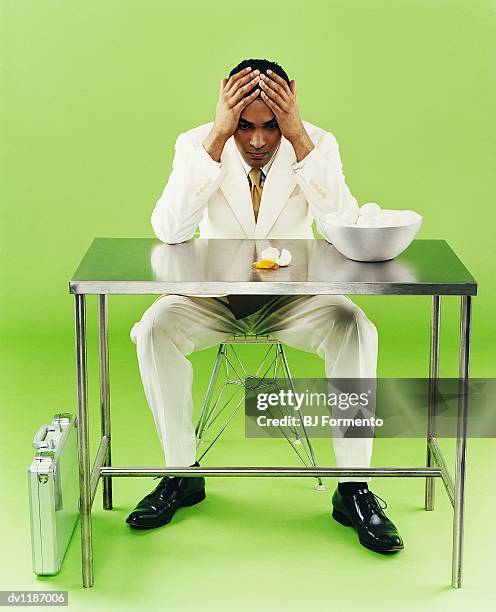 businessman looking down at a broken egg sitting on chair behind a metallic desk - broken chair stock pictures, royalty-free photos & images