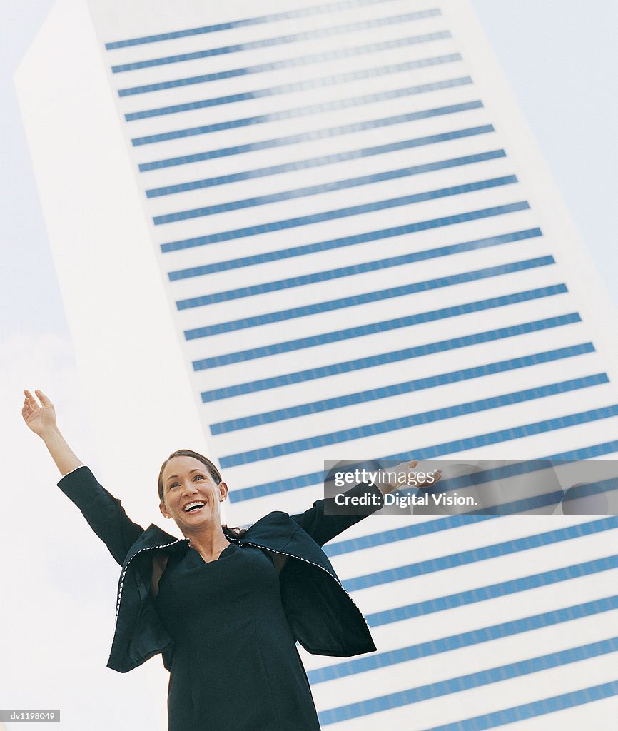 Happy Businesswoman With Her Arms Up Standing in Front of a Modern Building