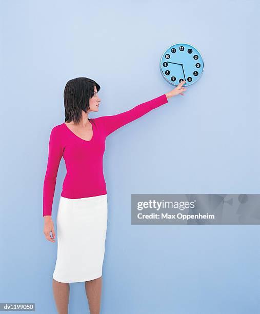 young businesswoman adjusting the minute hand on a wall clock - horloge murale photos et images de collection