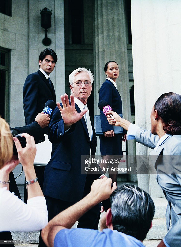 Man in a Suit Escaping From Cameramen and TV Reporters by a Building