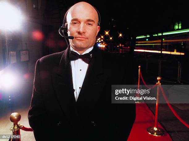 portrait of a bouncer wearing a headset standing on a red carpet at night - doorman stockfoto's en -beelden