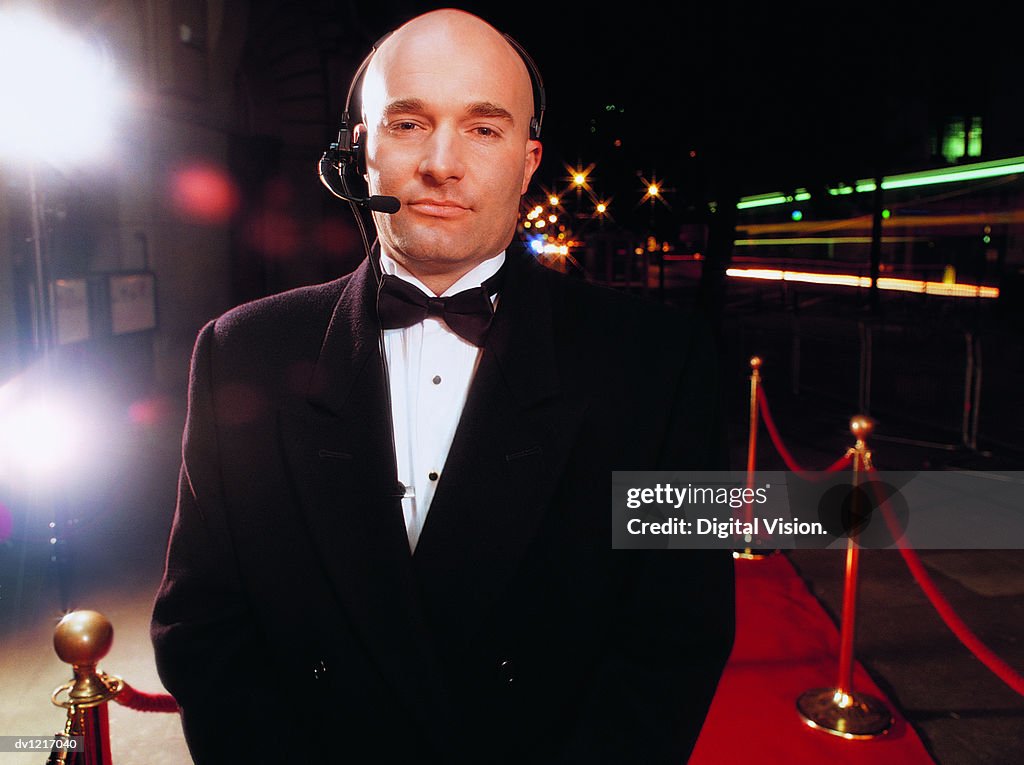 Portrait of a Bouncer Wearing a Headset Standing on a Red Carpet at Night