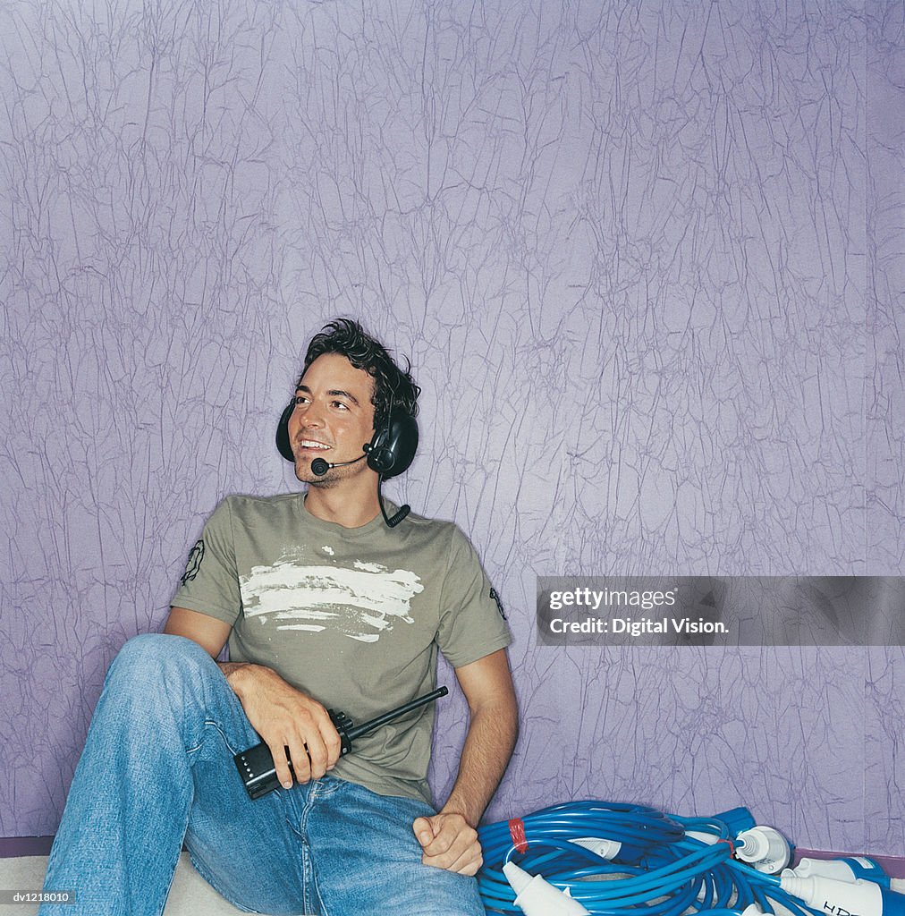 Young Male Tv industry Technician Sitting Holding a Walkie Talkie and Wearing Headphones