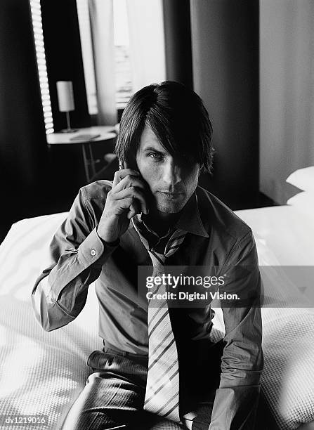 businessman sitting on the edge of a bed in a hotel room using his mobile phone - wonky fringe stock pictures, royalty-free photos & images