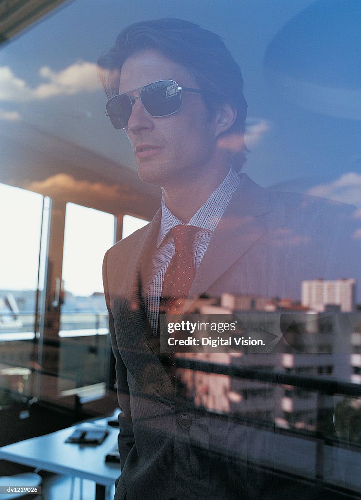 Businessman Wearing Sunglasses Looking Out of an Office Window
