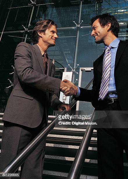 businessmen outdoors shaking hands on a stairway - low angle view of two businessmen standing face to face outdoors stock pictures, royalty-free photos & images