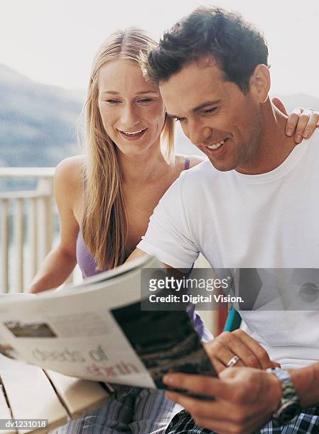 couple sitting reading a magazine amused, woman with arm around man - magazine retreat day 2 stock pictures, royalty-free photos & images