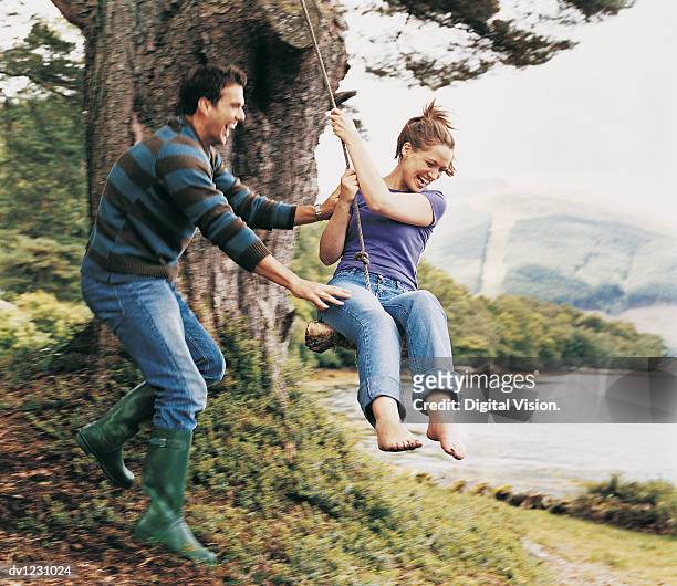 couple playing on a rope swing, man pushing woman - couple swinging stock pictures, royalty-free photos & images