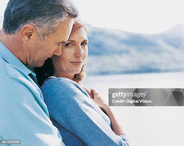 mature couple stand together beside lake, woman looking at camera - met de neus aanraken stockfoto's en -beelden