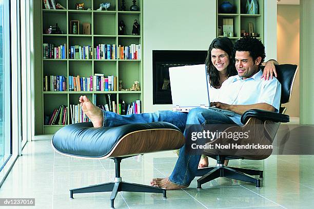 man sitting in a chair using a laptop and a woman with her arm around him watching - taburete pequeño fotografías e imágenes de stock