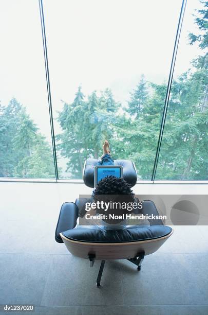 man sitting using laptop near window above forest - taburete pequeño fotografías e imágenes de stock