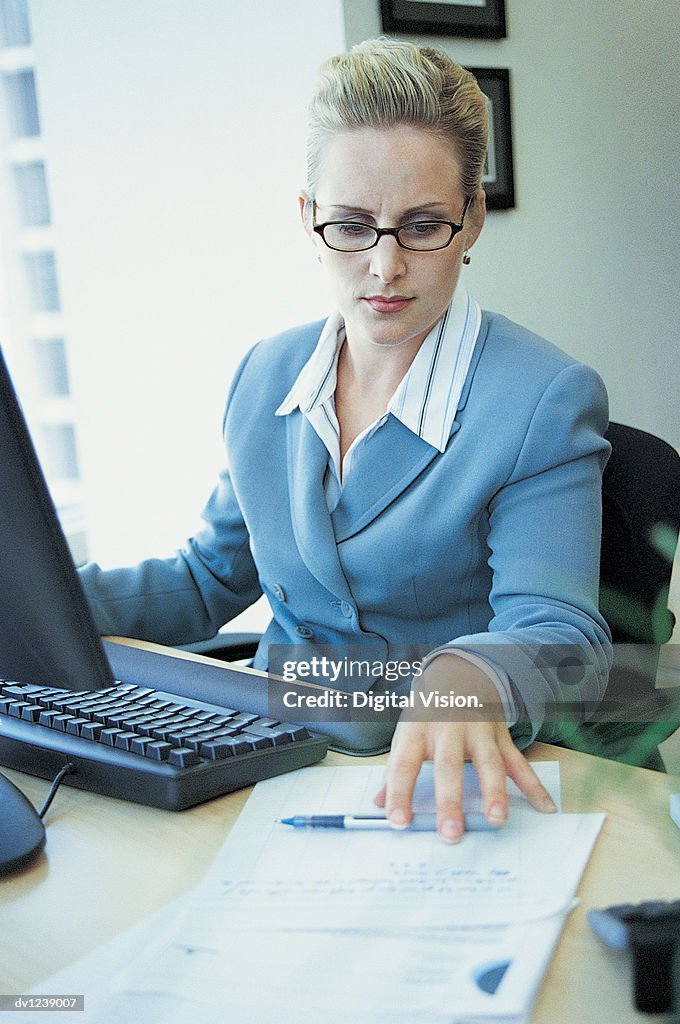 Businesswoman Reading a Document at Her Desk and Using a Computer