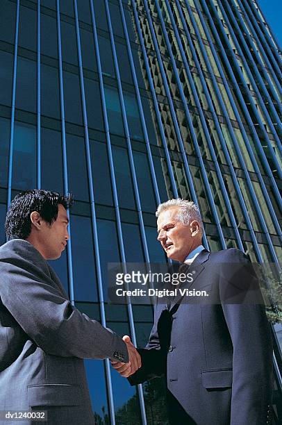 two businessmen shaking hands outside a skyscraper in a city - low angle view of two businessmen standing face to face outdoors stock pictures, royalty-free photos & images