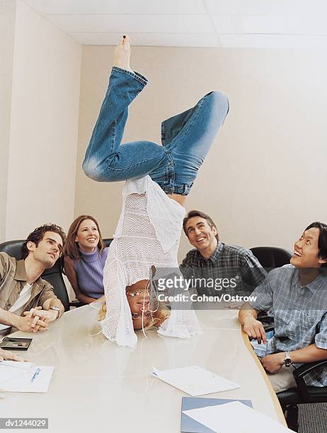 businesswoman doing a handstand on a table in a conference room to the amusement of her colleagues - businesswoman handstand stock pictures, royalty-free photos & images