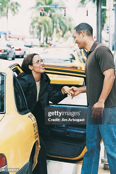 casually dressed man helping a businesswoman to get out of a yellow taxi - get stock pictures, royalty-free photos & images