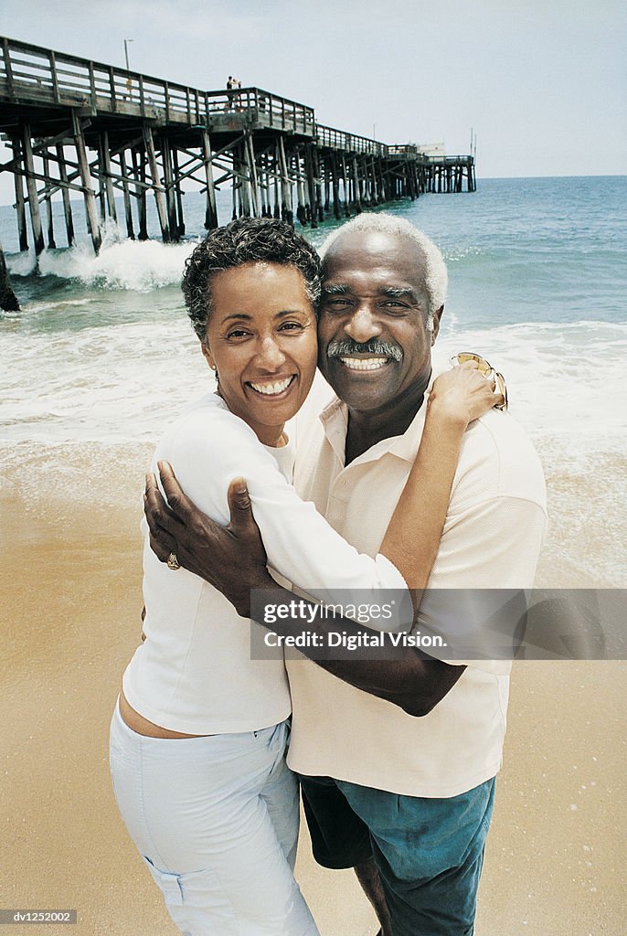 Portrait of a Couple With Their Arms Around Each Other Standing on a Beach by a Pier