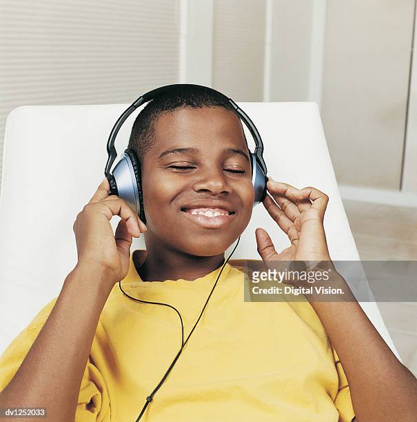 teenage boy sitting in an armchair listening to a cd with his eyes closed - young boy enjoying music stock-fotos und bilder