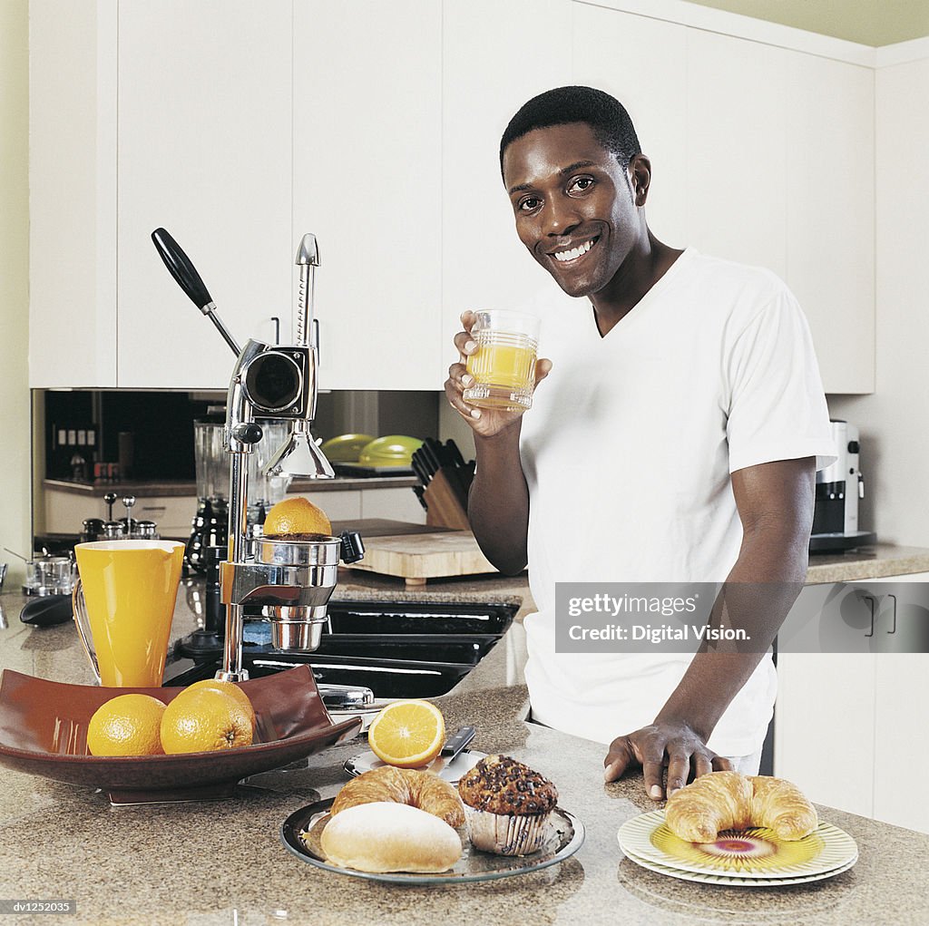Young Man Standing at a Kitchen Counter Holding a Glass of Orange Juice