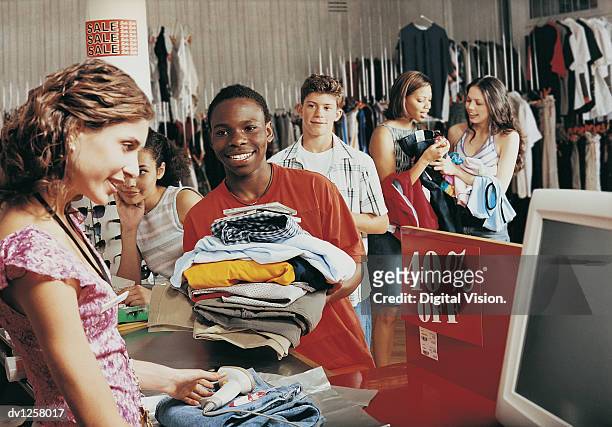 young boy buying a stack of clothing from a shop assistant at a checkout counter in a clothes shop - commercial event 個照片及圖片檔