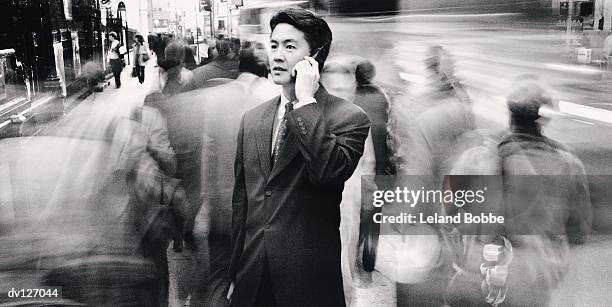 asian businessman on cell phone on busy city sidewalk - leland bobbe foto e immagini stock