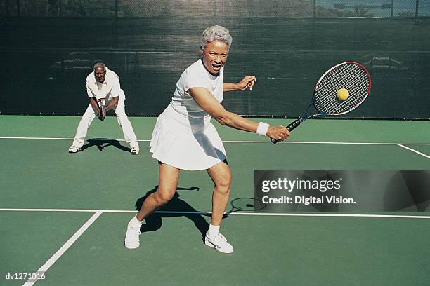 senior woman hitting a tennis ball on a tennis court and a senior man standing behind - tennis woman photos et images de collection