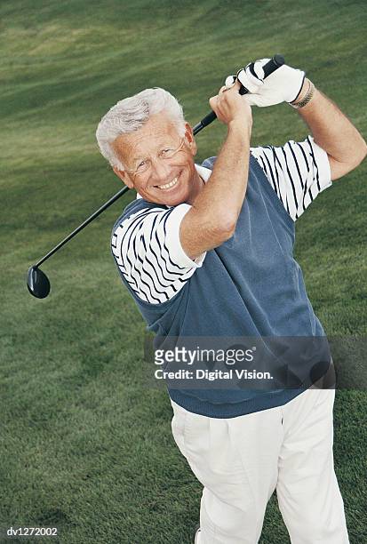 portrait of a smiling, senior adult swinging a golf club on a golf course - senior golf swing stock pictures, royalty-free photos & images