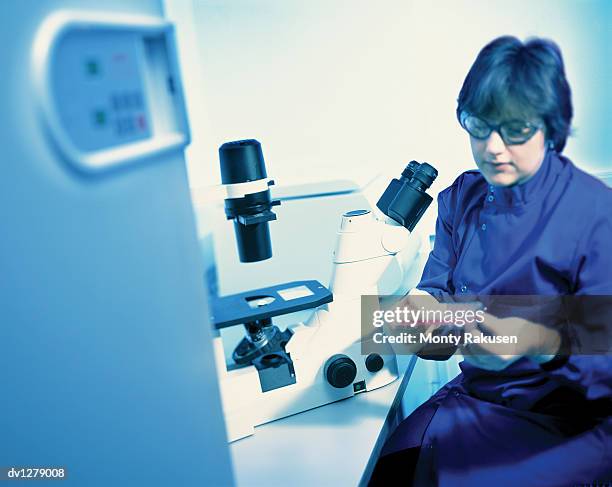 scientist holding a dna medical sample and sitting by a microscope on a desk - medical sample stock-fotos und bilder